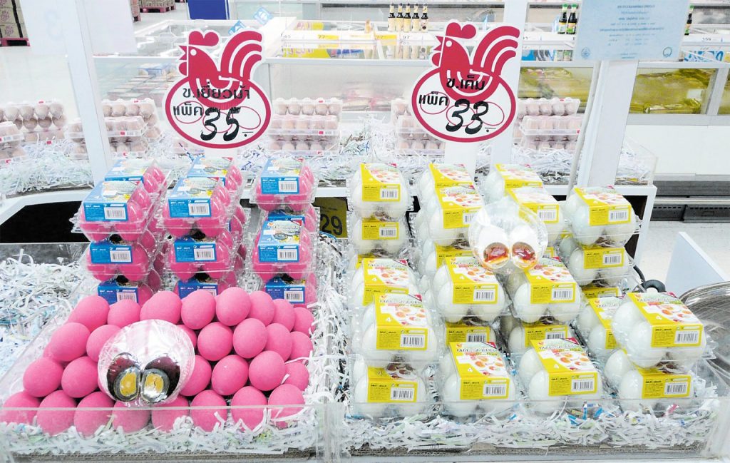 Verkaufsstand mit bunten Eiern: links pink gefärbte, rechts weiße und gelb verpackte Eier. Schilder mit Hahnenmotiven und Preisen in asiatischer Schrift.