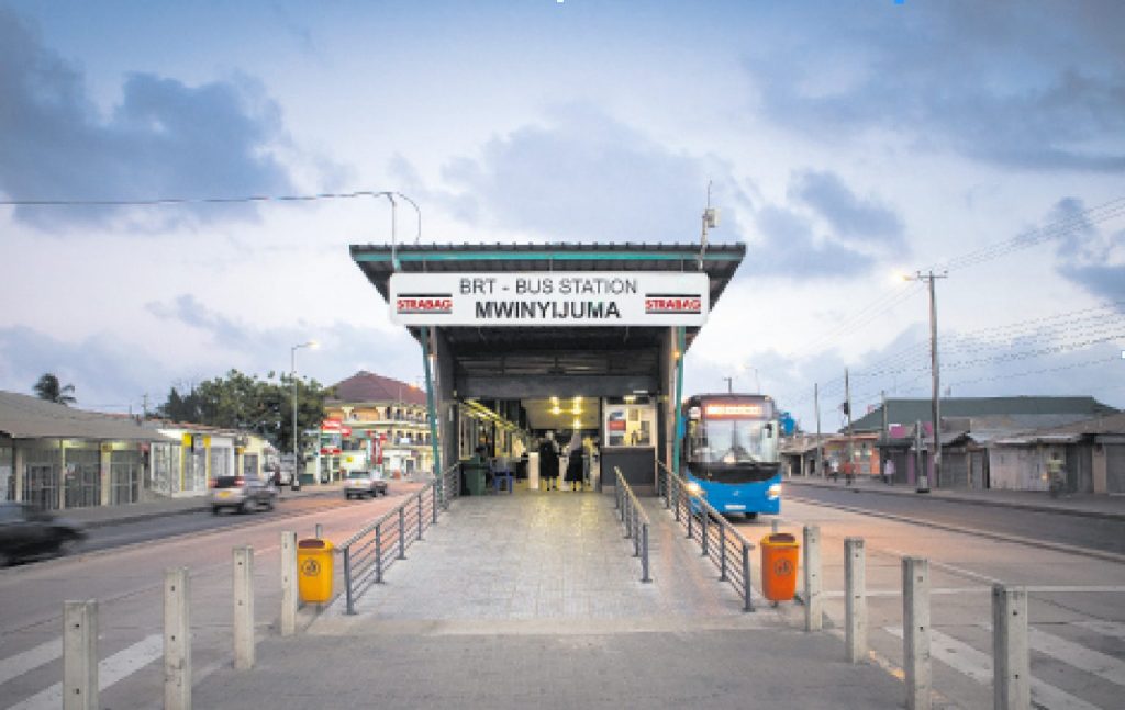 Busstation Mwinyijuma mit blauem Linienbus, überdachtem Bahnsteig und wenigen wartenden Passagieren.