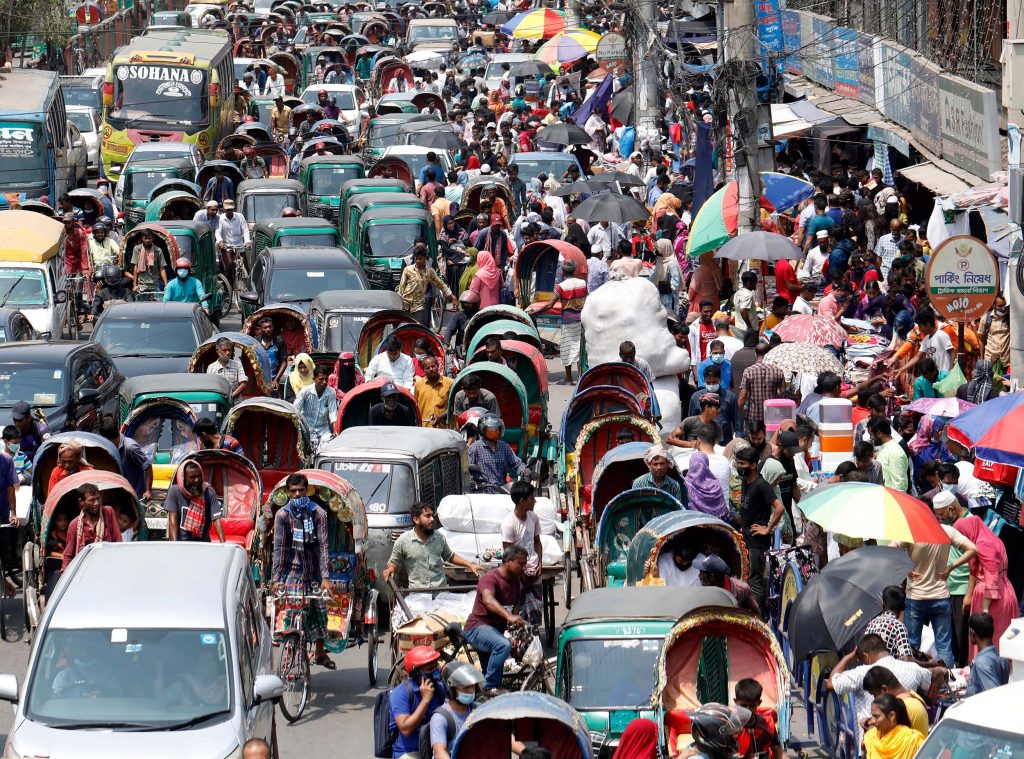 Dicht gedrängter Verkehr mit Autos, Rikschas und vielen Fußgänger:innen auf einer belebten Straße in Bangladesch.